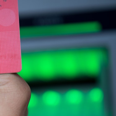 Eine Person hält vor einem Geldautomaten eine Girocard in der Hand. Auf der Karte ist das Maestro-Logo zu sehen.