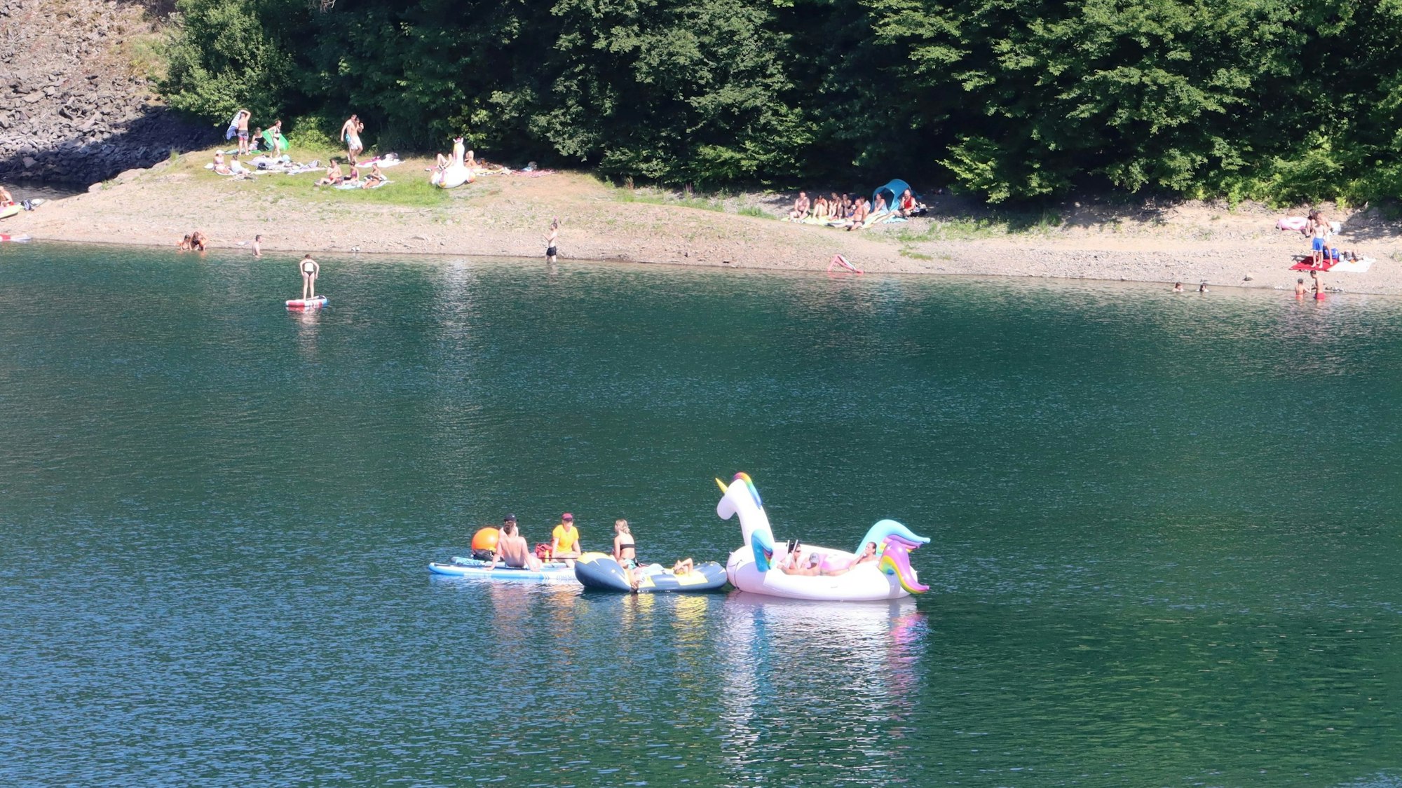 Menschen beim Baden in der Aggertalsperre. Einige liegen auf aufblasbaren Badetieren auf dem Wasser.