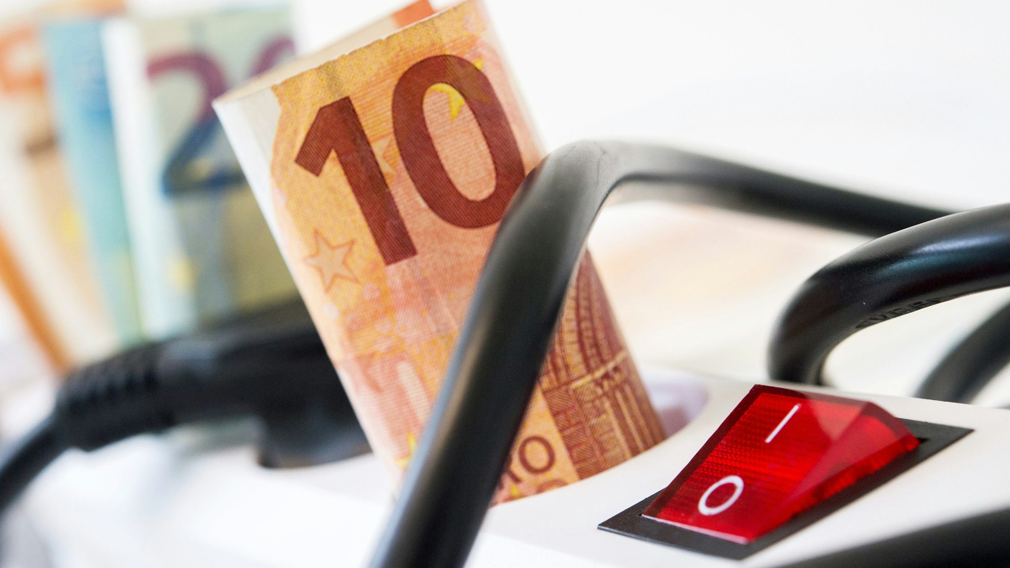 Eine Steckerleiste, in der statt Steckern gerollte Geldscheine stecken. (Symbolbild)