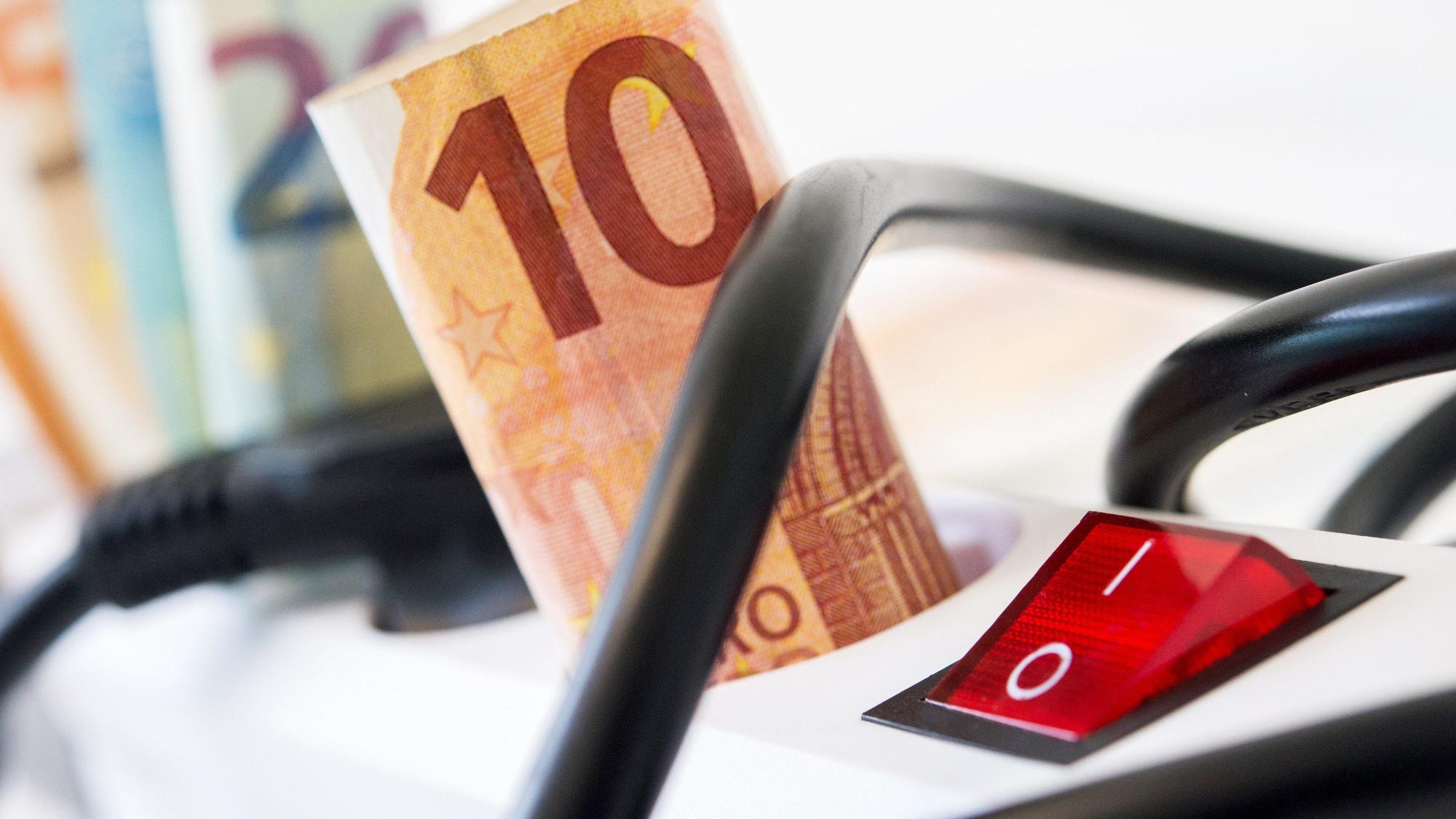 Die Strompreise sollen noch einmal deutlich steigen. Unser Symbolfoto zeigt Geldscheine in einer Steckerleiste.