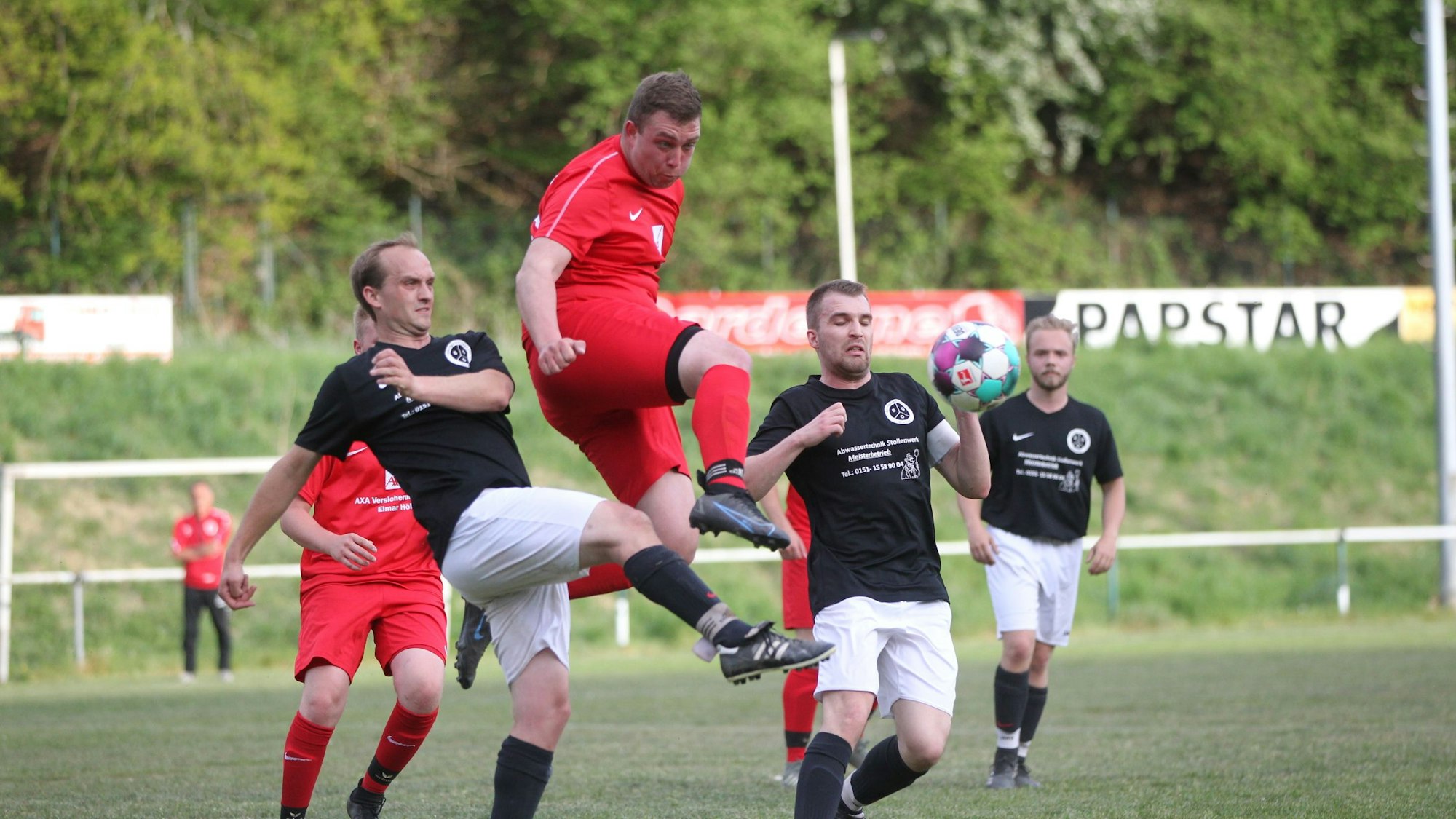 Mehrere Fußballspieler mit roten und schwarzen Trikots kämpfen um den Ball.
