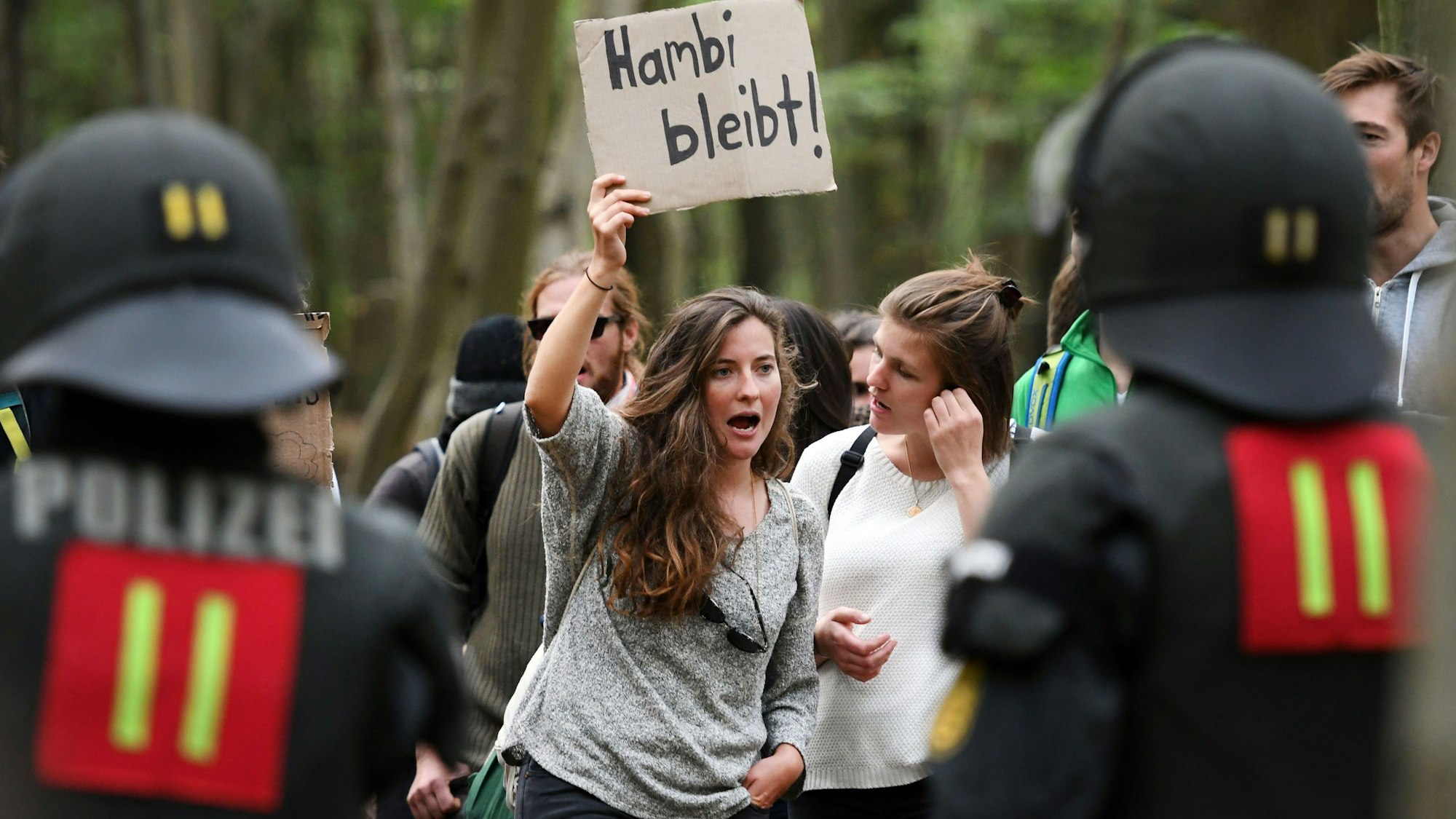 ARCHIV - 15.09.2018, Nordrhein-Westfalen, Kerpen: Teilnehmer einer Demonstration gegen die Räumung und die geplante Rodung des Hambacher Forstes halten in der Nähe des Baumhausdorfes «Oaktown» eine Kundgebung ab. Eine Demonstrantin zeigt ein Schild mit den Worten «Hambi bleibt!». Die Polizei hatte am 13. September 2018 damit begonnen, den Wald zu räumen. (zu dpa: «Räumung Hambacher Forst: NRW-OVG verhandelt zum Brandschutz») Foto: Henning Kaiser/dpa +++ dpa-Bildfunk +++