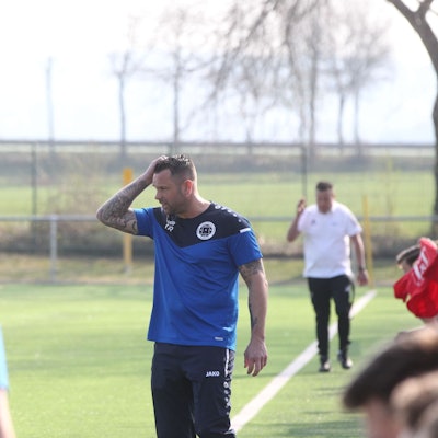 DHO-Trainer Gerrit Ueckert steht an der Seitenlinie, beobachtet das Spiel und fährt sich mit der rechten Hand durch die Haare.