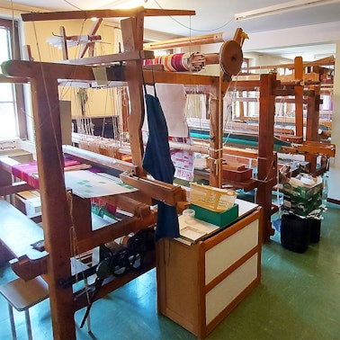 Sechs alte Handwebstühle stehen in einem Saal eines ehemaligen Klosters.