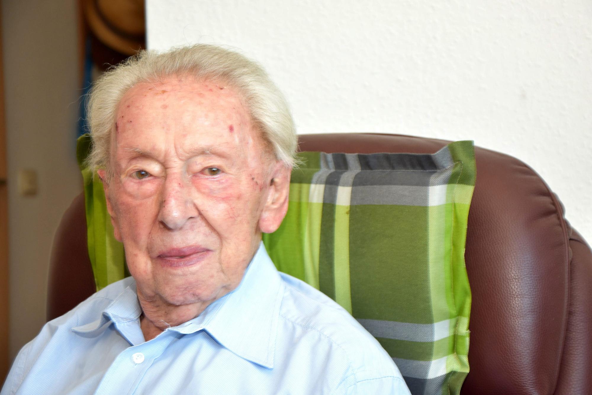 Heinz Ollig wird heute 103 Jahre alt. Er schaut an der Kamera vorbei, sitzt dabei auf einem braunen Sessel.