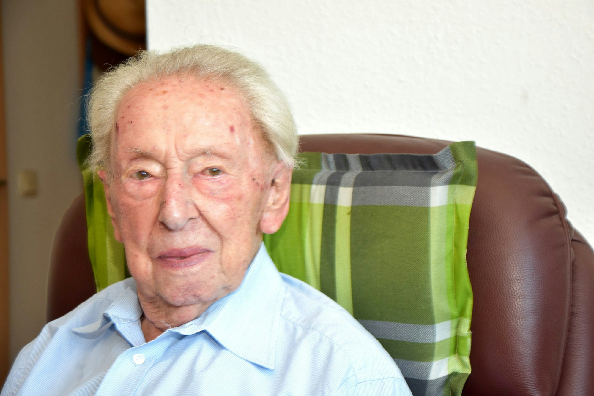 Heinz Ollig wird heute 103 Jahre alt. Er schaut an der Kamera vorbei, sitzt dabei auf einem braunen Sessel.