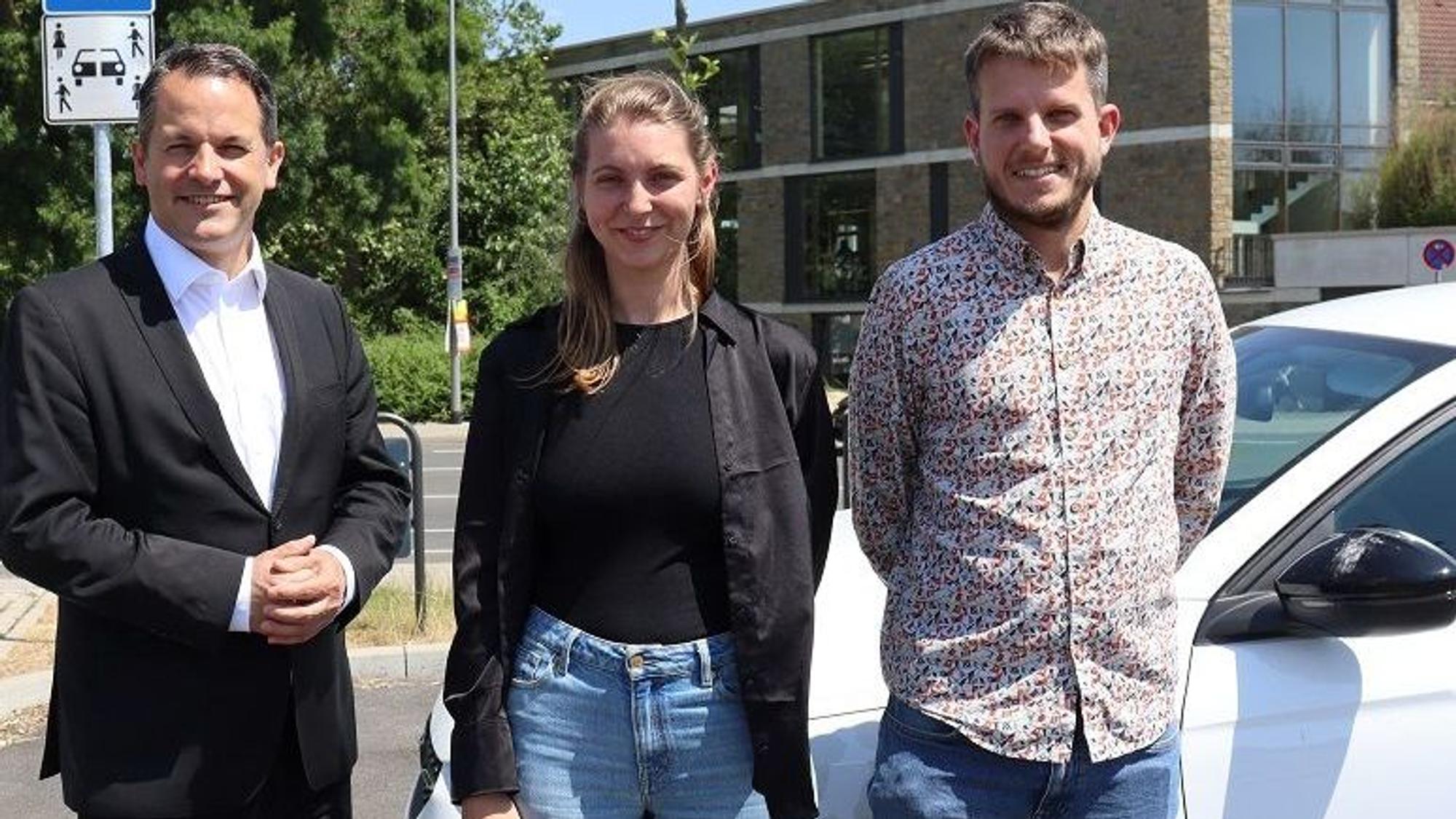 Bürgermeister Frank Keppeler (v.l.) hat sich mit Klimaschutzmanagerin Jana van Kranenbrock und Mobilitätsmanager Thomas Bette ein Bild vor Ort gemacht. Alle drei schauen, vor einem Auto stehend, in die Kamera.