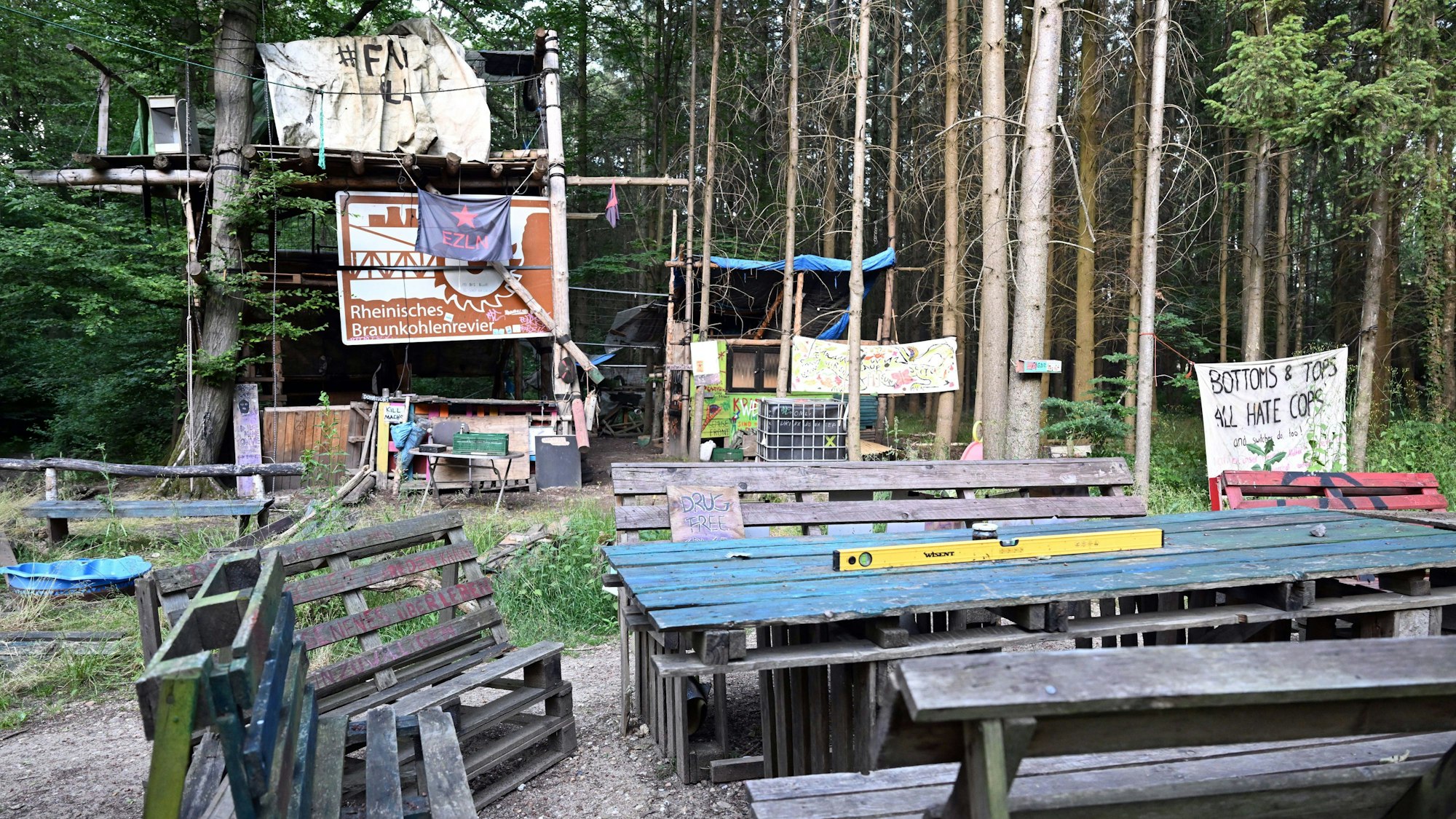 Verlassene Baumhäuser stehen im Hambacher Forst hinter leeren Tischen und Bänken. Mit der Räumung des Hambacher Forsts im Jahr 2018 beschäftigt sich am Freitag (16.06.2023) das nordrhein-westfälische Oberverwaltungsgericht in Münster.