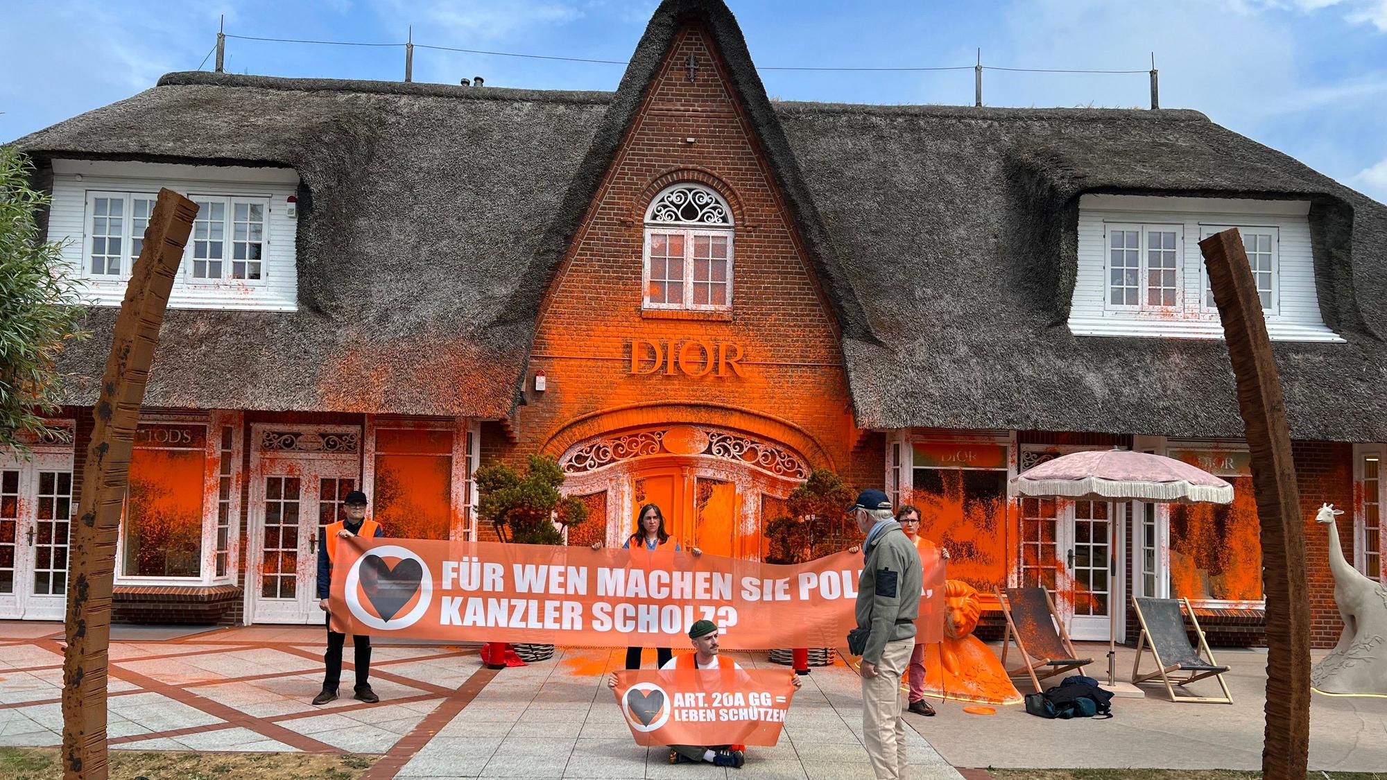 Klima-Aktivisten haben sich vor einem besprühten Luxusgeschäft auf der Insel Sylt platziert