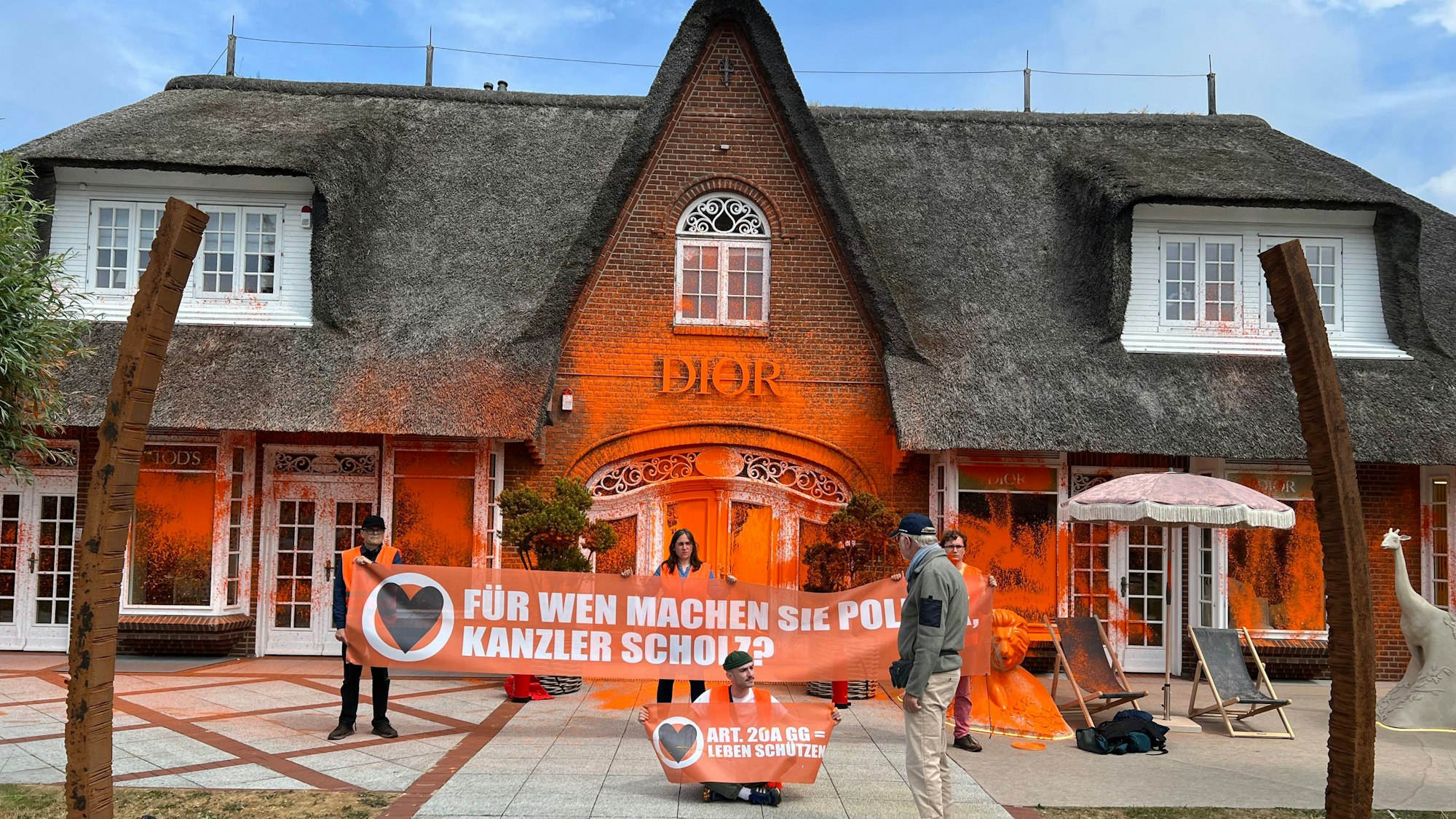Klima-Aktivisten haben sich vor einem besprühten Luxusgeschäft auf der Insel Sylt platziert