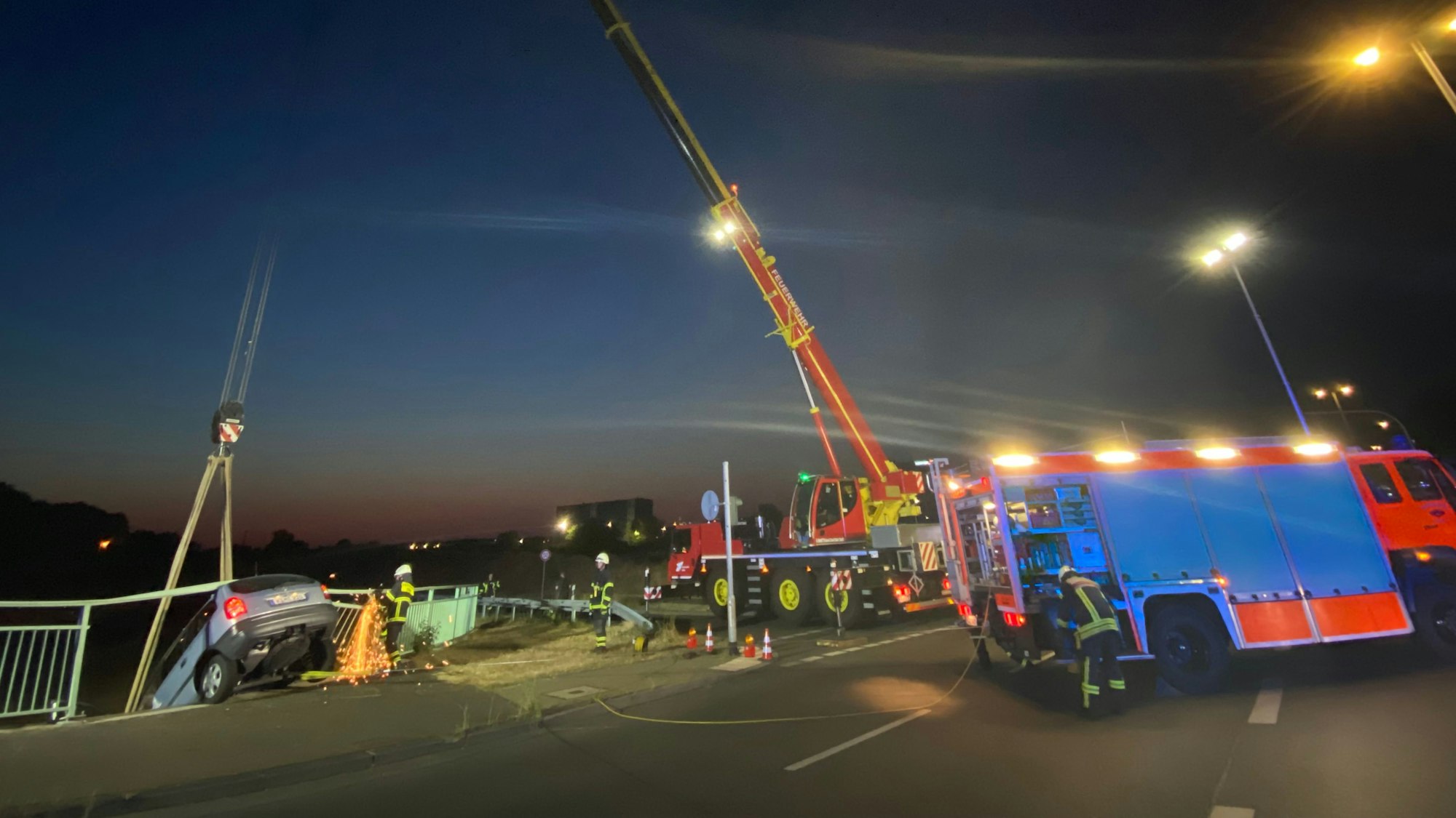 Die Kölner Feuerwehr sichert ein Auto, das zuvor die Brüstung auf der Brücke der Merianstraße in Köln-Merkenich durchbrochen hat. Der Fahrer blieb unverletzt.