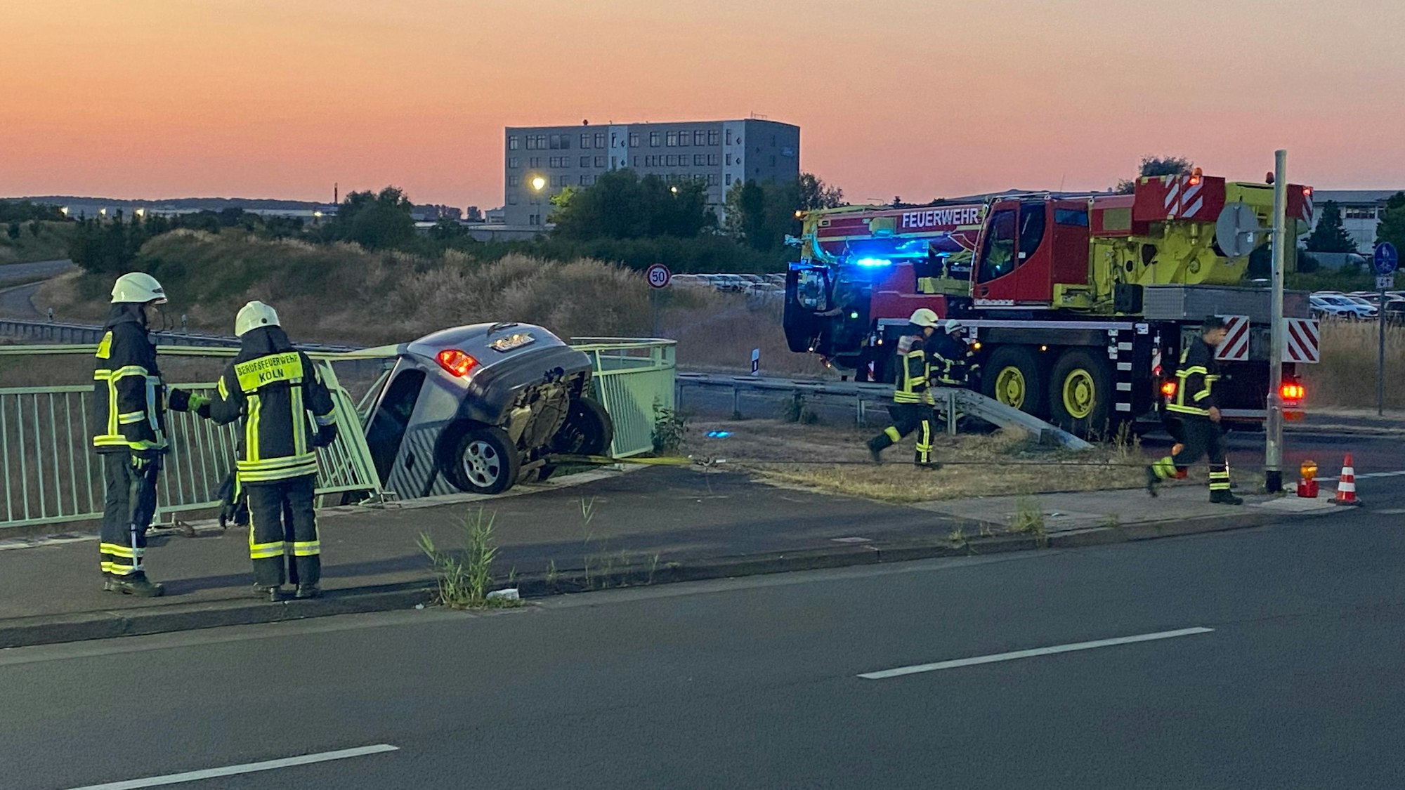 Ein Auto hängt an der Brüstung der Brücke der Merianstraße in Köln-Merkenich. Der Fahrer blieb bei dem Unfall am Freitagabend unverletzt.