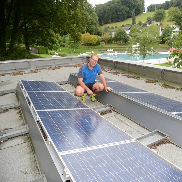 Ein Mann hockt zwischen Photovoltaik-Panelen auf dem Dach der Umkleiden des Hoffnungsthaler Freibads.