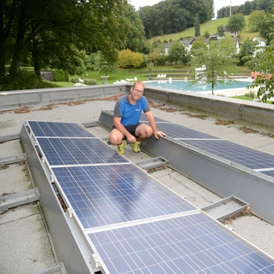 Ein Mann hockt zwischen Photovoltaik-Panelen auf dem Dach der Umkleiden des Hoffnungsthaler Freibads.