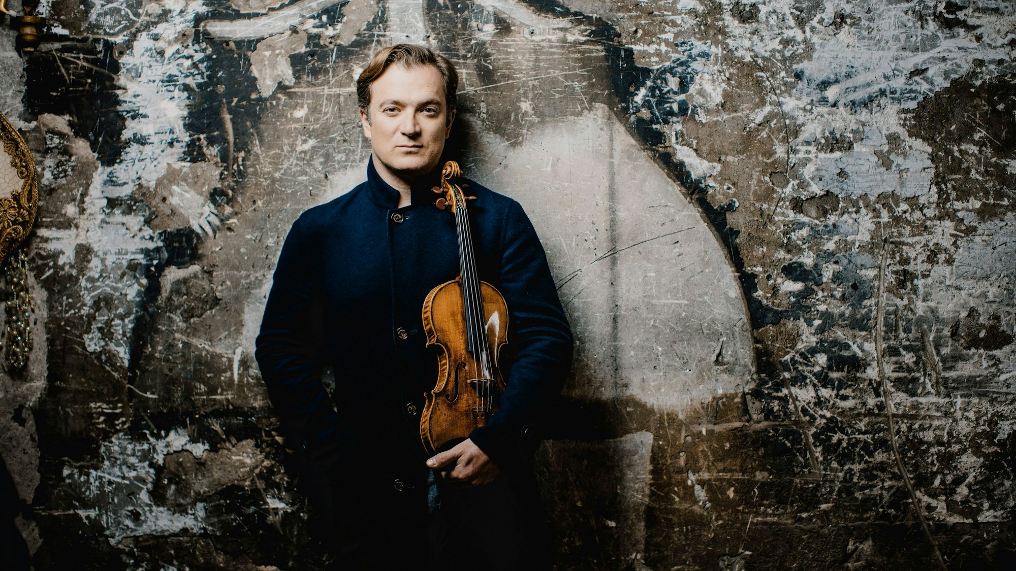 Renaud Capuçon steht vor einer Wand und hält eine Violine in der Hand.