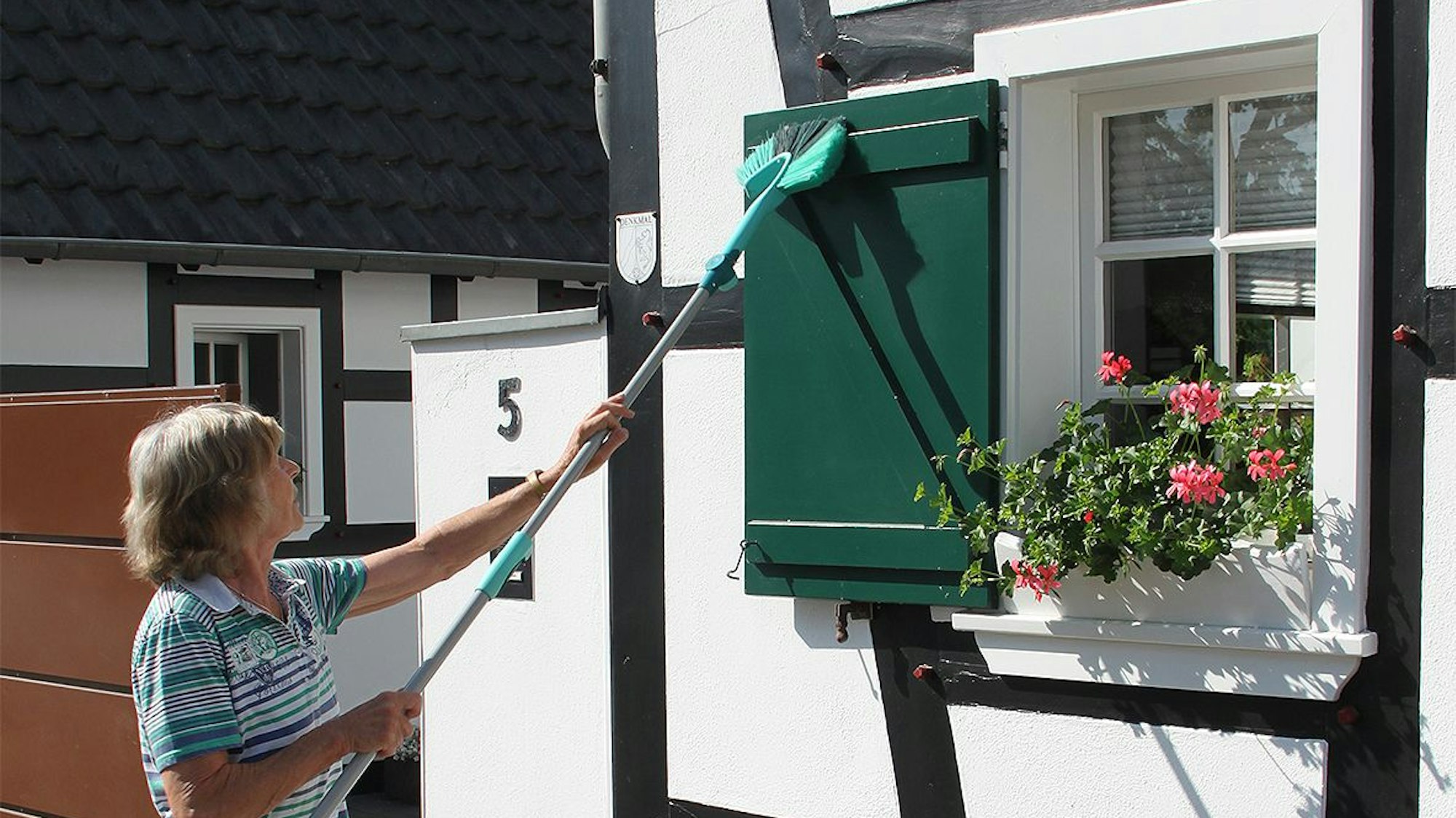 Eine Frau säubert die Fensterläden eines Fachwerkhauses.