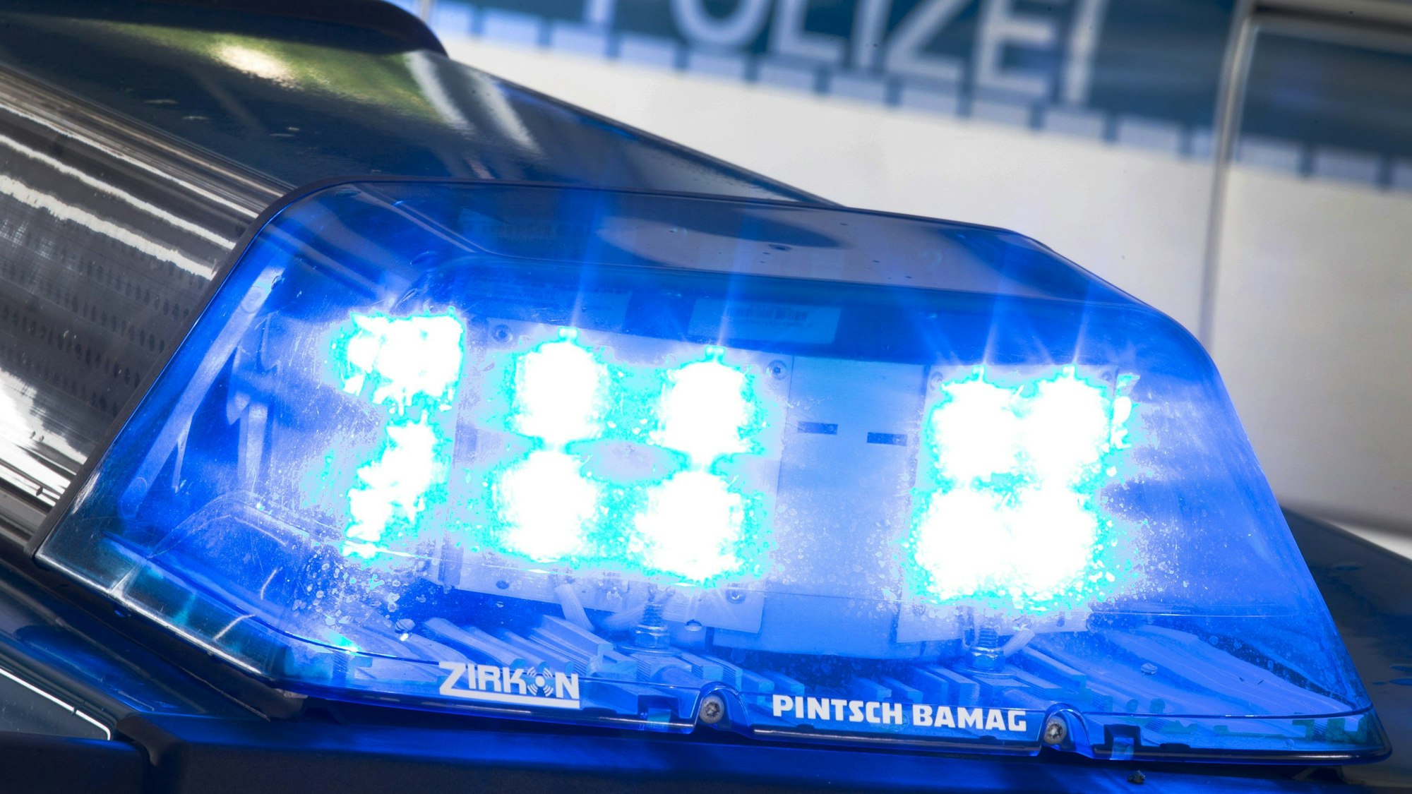 Ein Blaulicht leuchtet auf dem Dach eines Polizeiwagens. Im Hintergrund steht ein weiterer Streifenwagen. (Symbolbild)