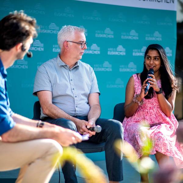 Zwei Männer und eine Frau diskutieren bei einer Podiumsveranstaltung.
