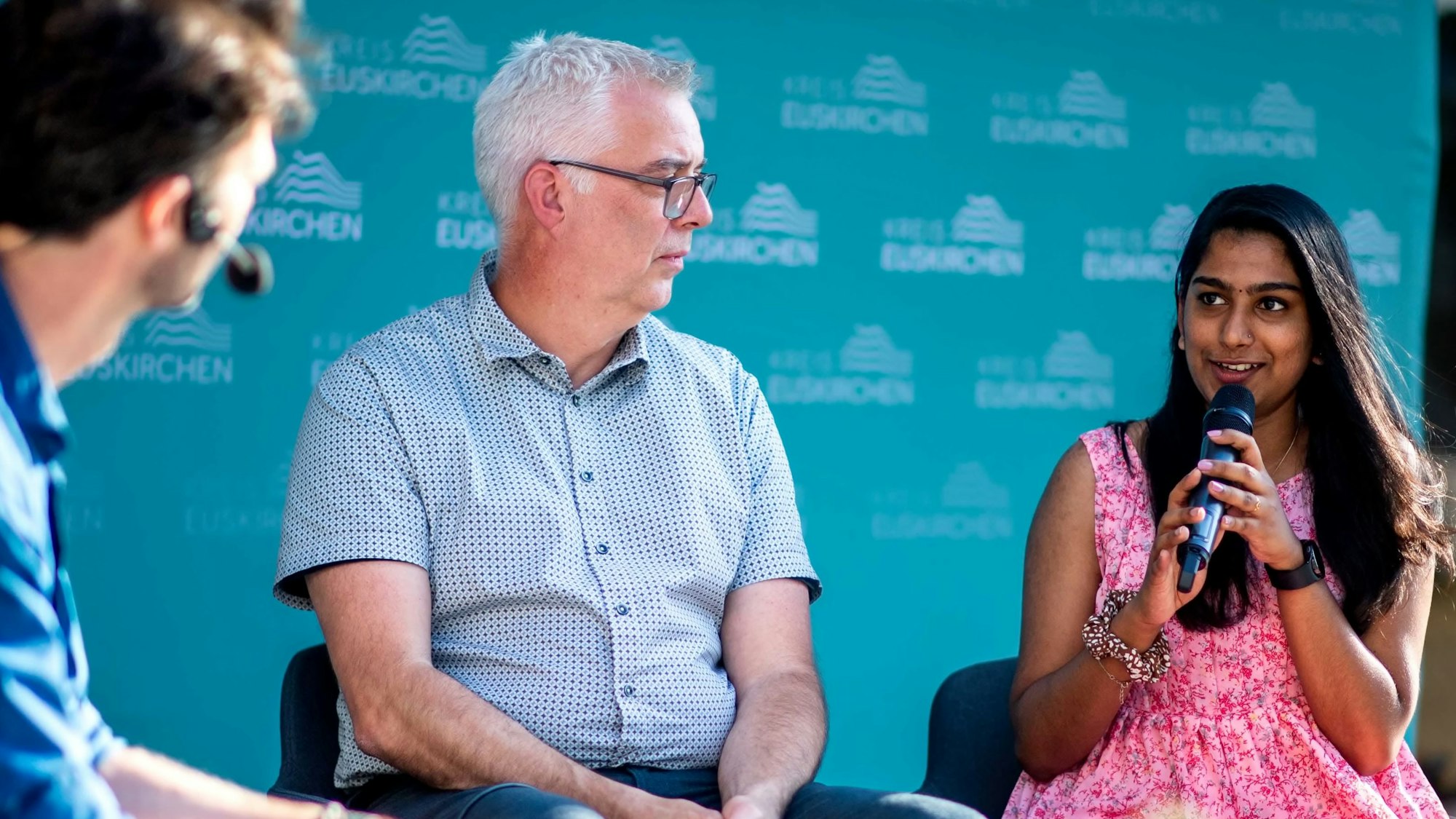 Zwei Männer und eine Frau diskutieren bei einer Podiumsveranstaltung.
