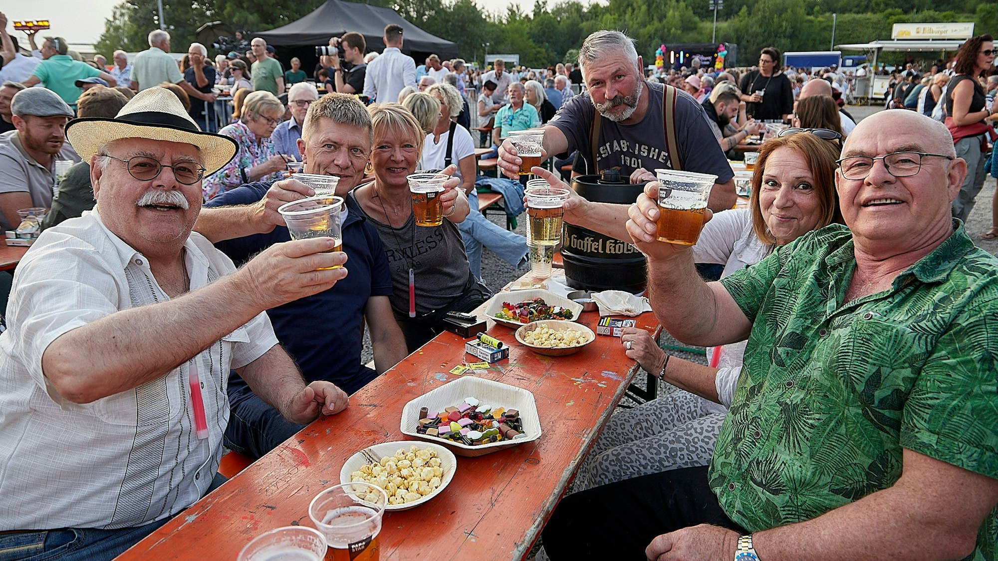 Besucher der Kaller Oldienacht sitzen an einem Biertisch und prosten in die Kamera.