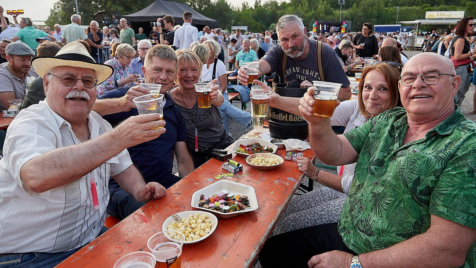 Besucher der Kaller Oldienacht sitzen an einem Biertisch und prosten in die Kamera.