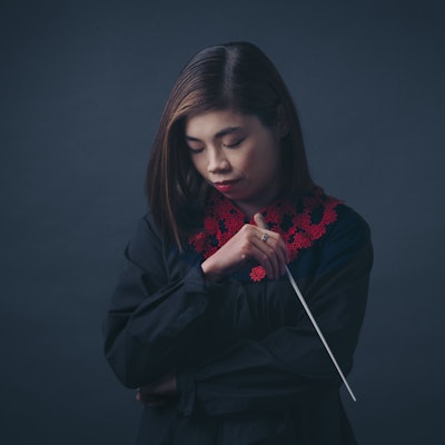 Elim Chan blickt zu Boden, in der linken Hand hält sie einen Dirigierstab.