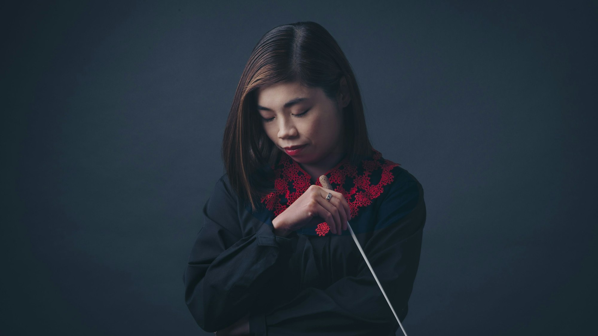 Elim Chan blickt zu Boden, in der linken Hand hält sie einen Dirigierstab.