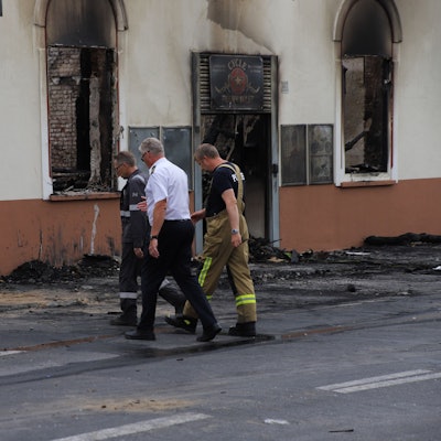 Drei Männer in Funktionskleidung gehen mit gesenkten Blicken auf das ausgebrannte Haus in Sankt Augustin zu.