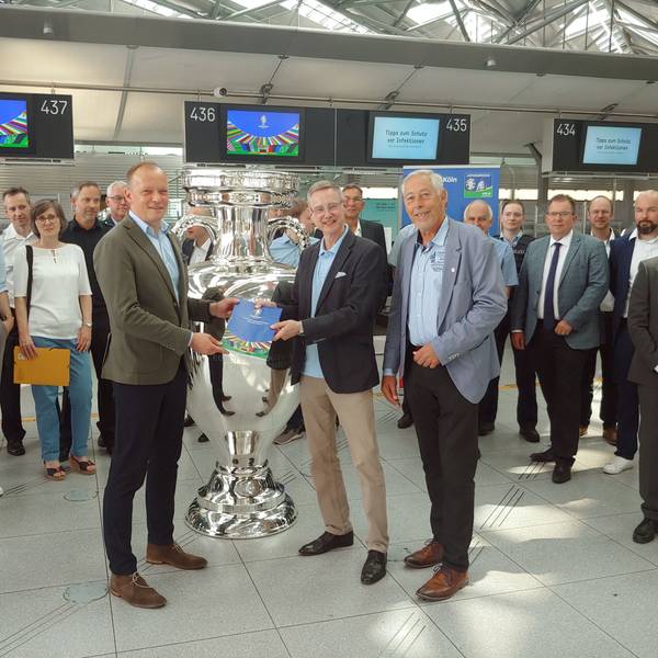 Die drei stehen mit anderen um einen silbernen Pokal