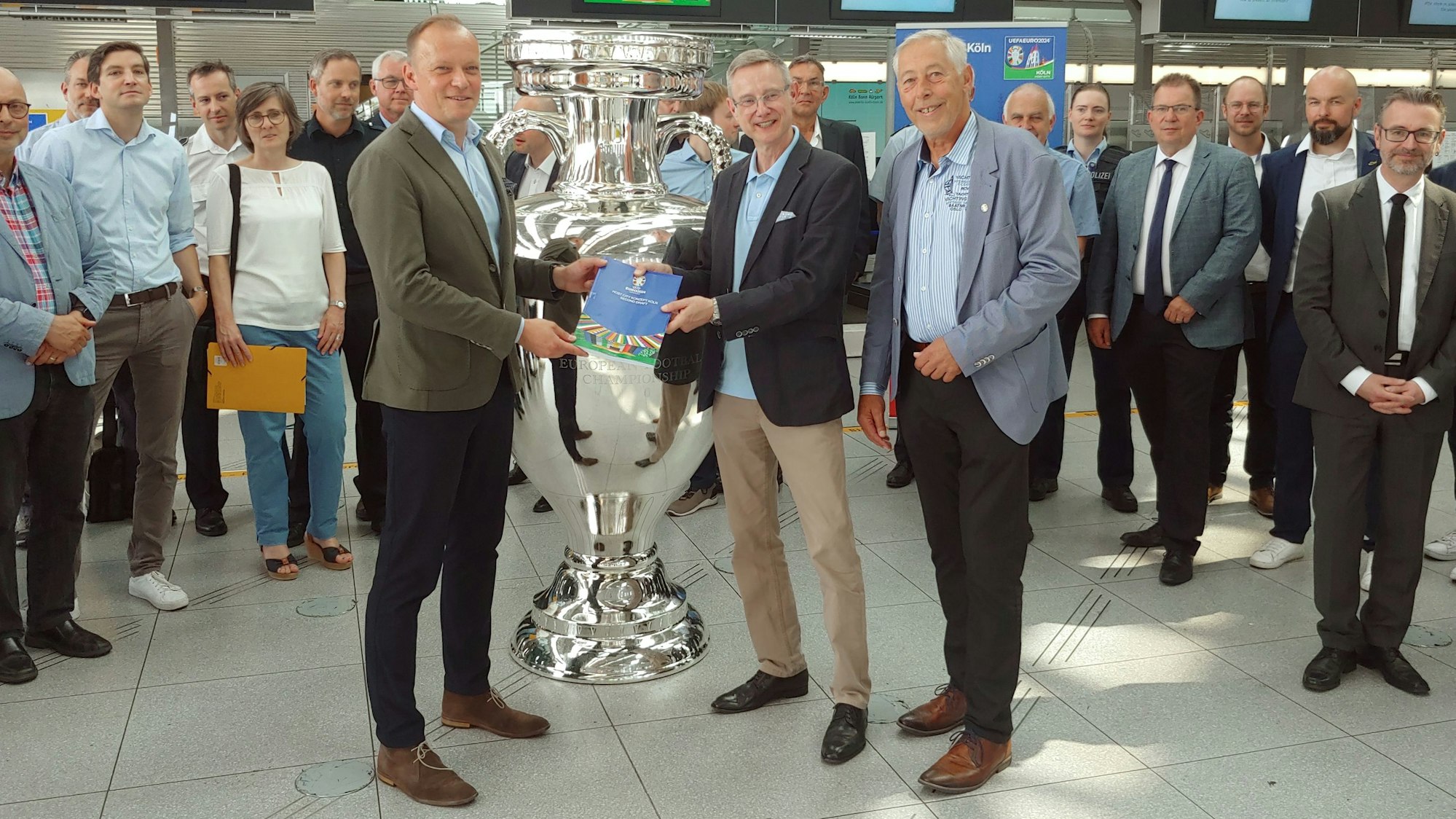 Die drei stehen mit anderen um einen silbernen Pokal