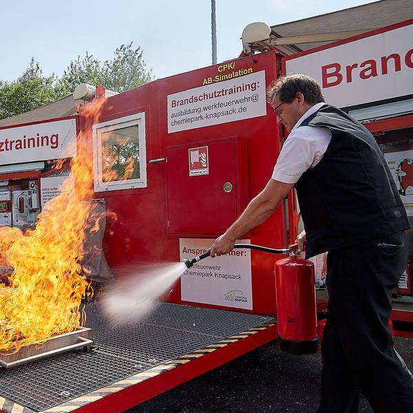 Ein Feuerwehrmann zielt mit einem Feuerlöscher auf eine Flamme.