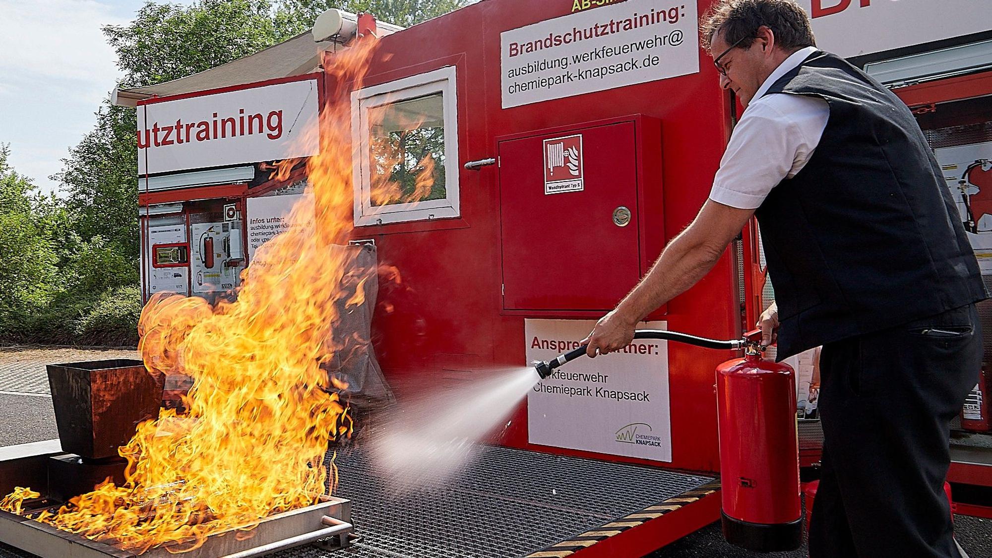 Ein Feuerwehrmann zielt mit einem Feuerlöscher auf eine Flamme.