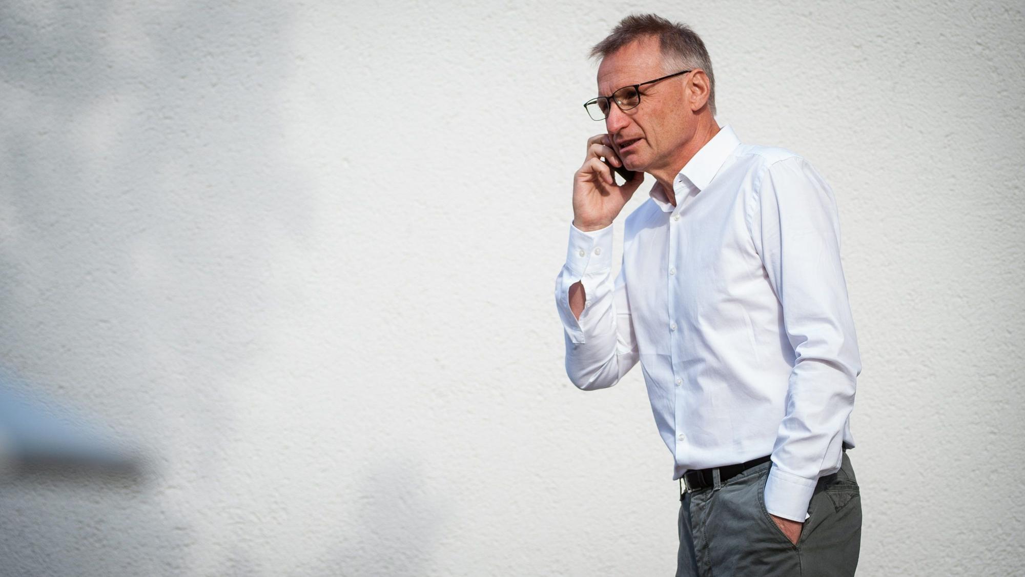 Der Fußballfunktionär Michael Reschke telefoniert mit der rechten Hand am Smartphone, hat die andere Hand in der Hosentasche.