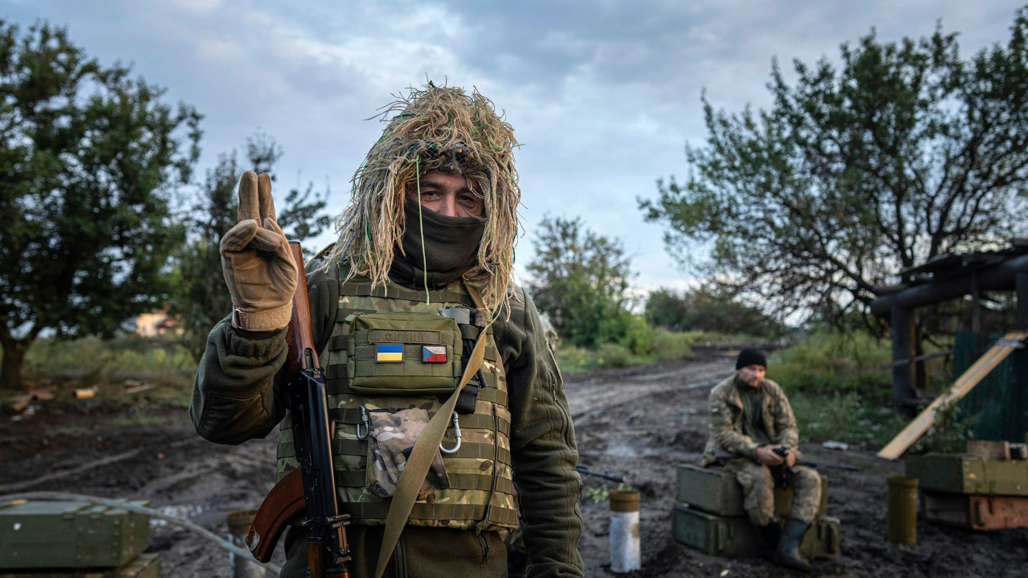 Ein ukrainischer Soldat zeigt ein Peace-Zeichen, während er seine Position am Kontrollpunkt bewacht. (Symbolbild)