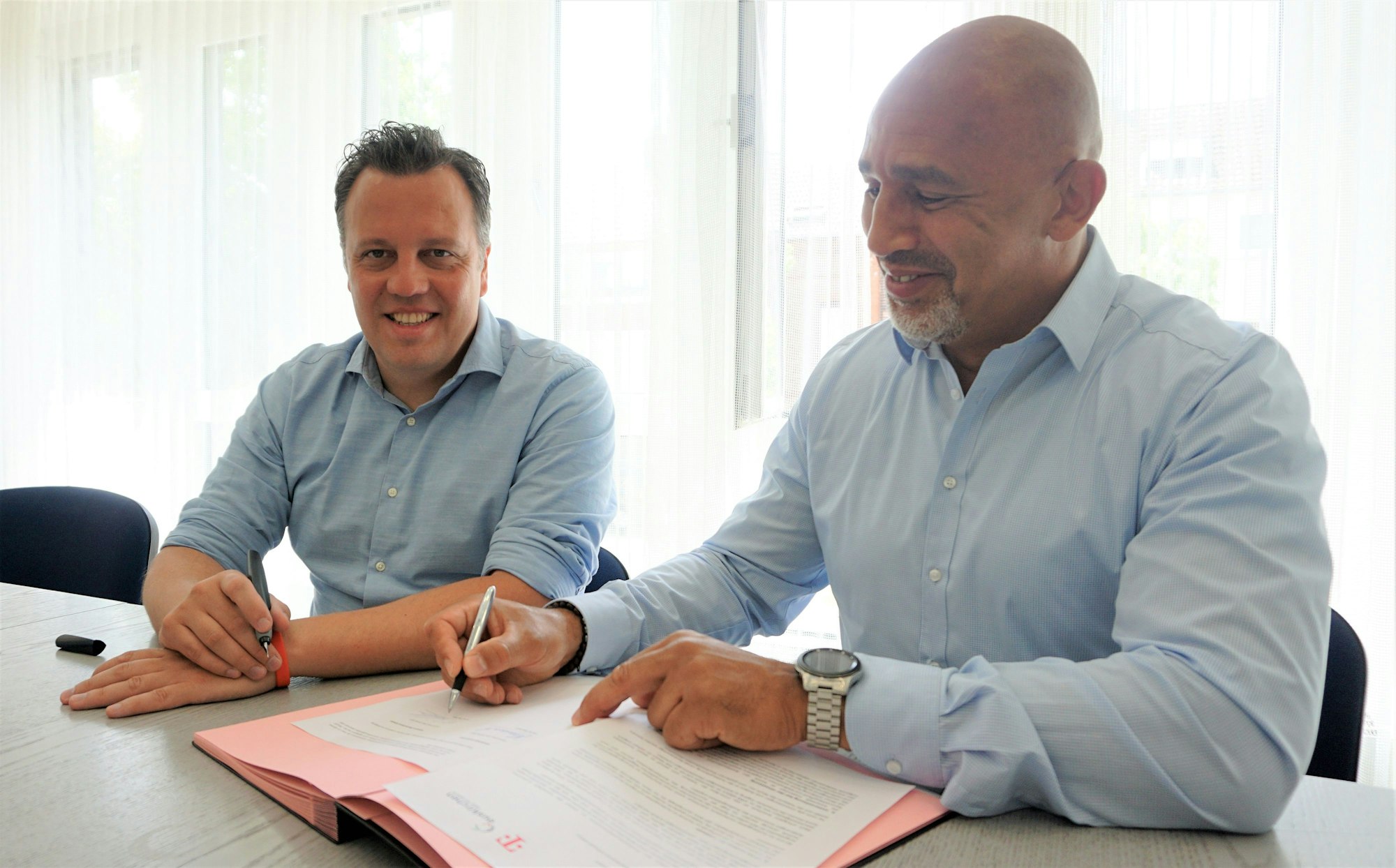 Bürgermeister Sacha Reichelt und Frank Pischke von der Telekom sitzen an einem Tisch im Euskirchener Rathaus und unterzeichnen Verträge zu Glasfaser-Ausbau in der Euskirchener Innenstadt.