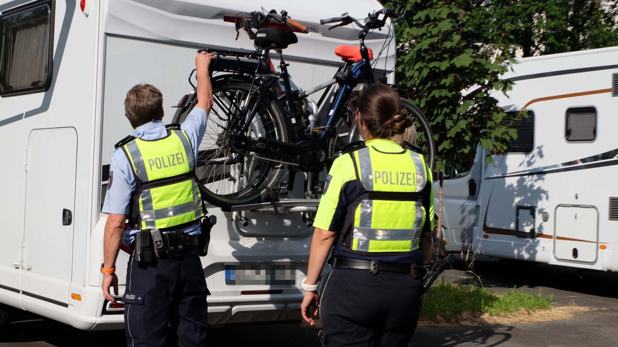 Auf dem Foto sind zwei Polizisten zu sehen, die überprüfen, ob Fahrräder an einem Wohnmobil ausreichend gesichert sind.