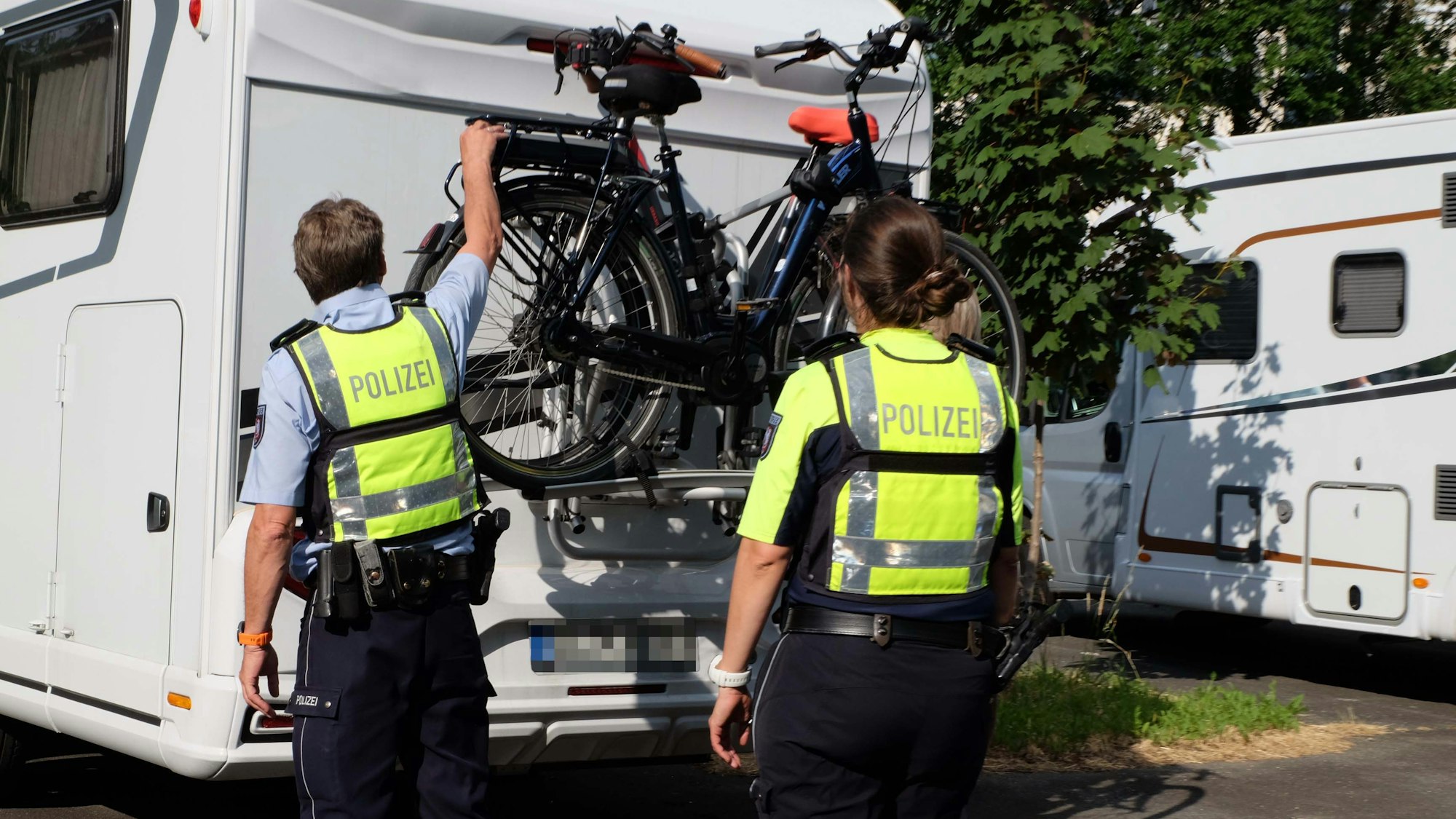 Auf dem Foto sind zwei Polizisten zu sehen, die überprüfen, ob Fahrräder an einem Wohnmobil ausreichend gesichert sind.