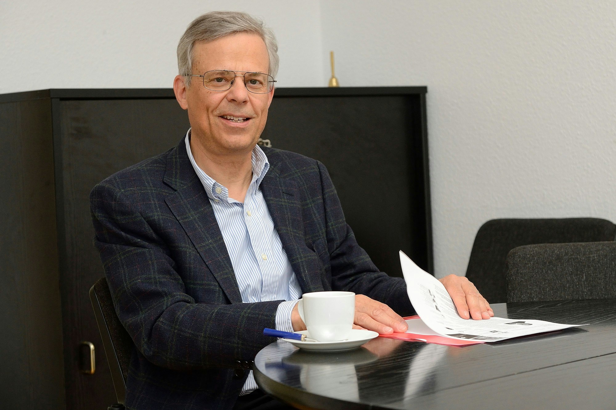 Jörg Krell sitzt an einem Schreibtisch, vor ihm liegen Papiere auf dem Tisch, neben einer Kaffeetasse.