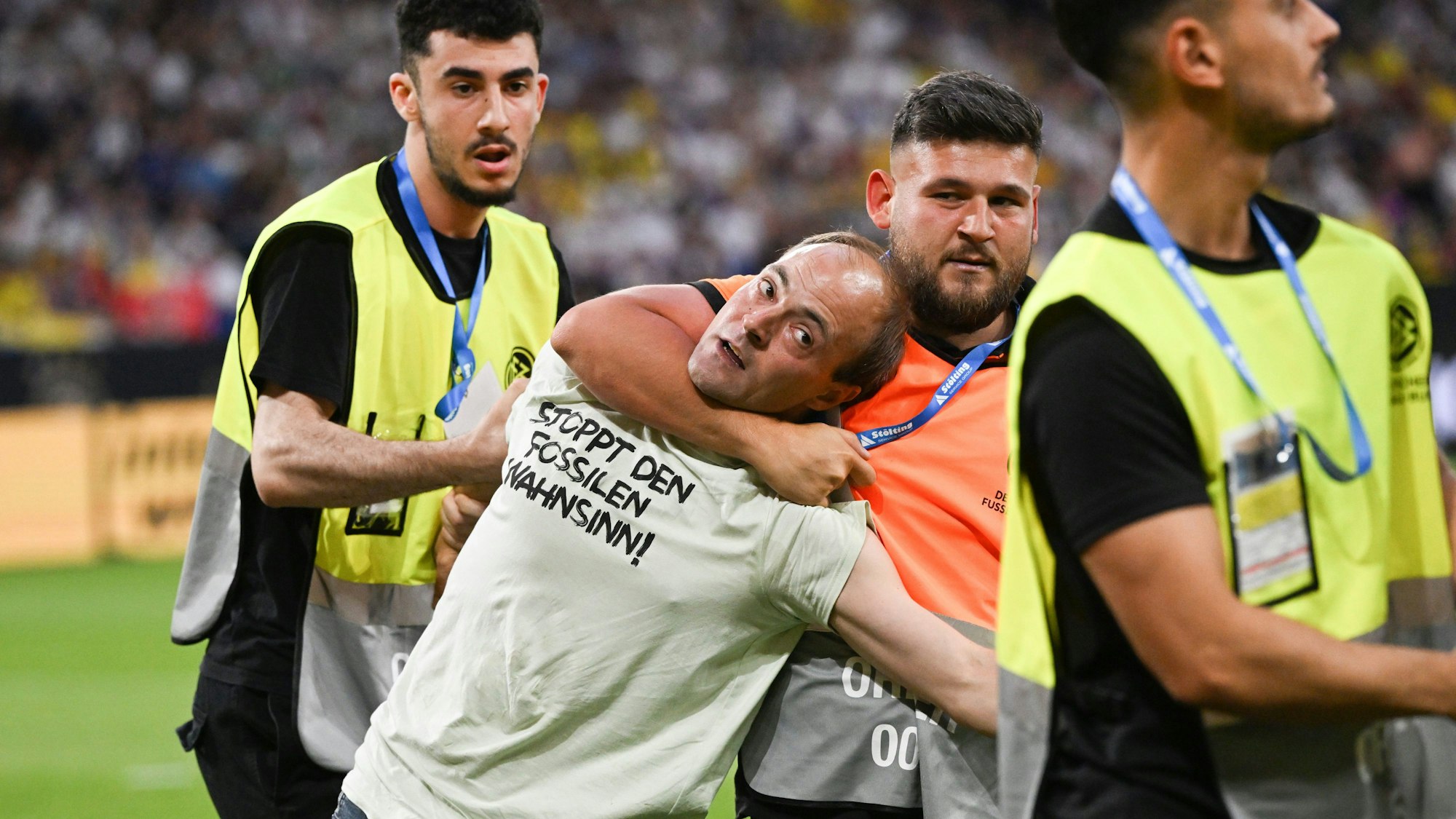 Eine Person, die auf das Spielfeld rannte und ein T-Shirt mit der Aufschrift „Stoppt den fossilen Wahnsinn!“ trägt, wird von Ordnern vom Feld geführt.