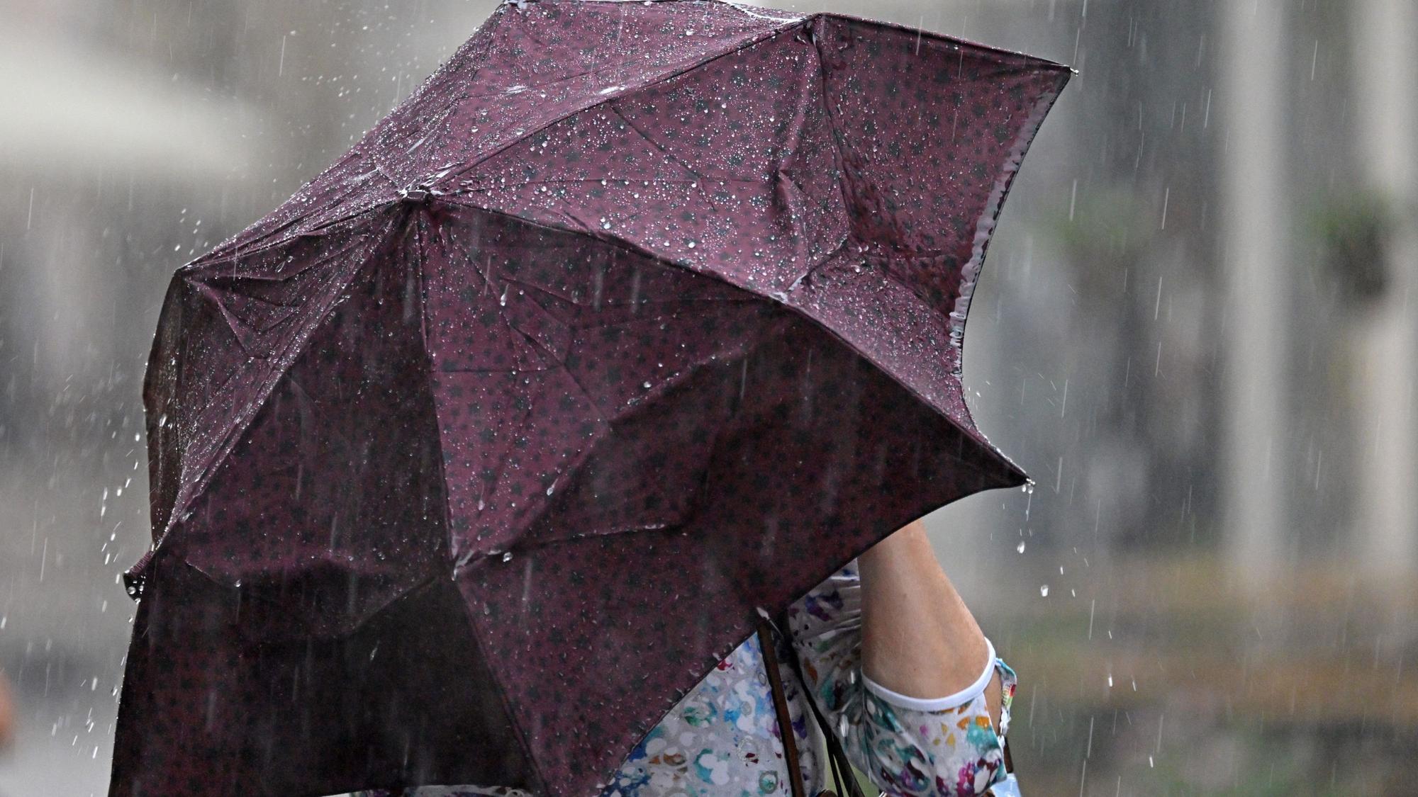 Eine Frau mit Regenschirm läuft durch den Starkregen.