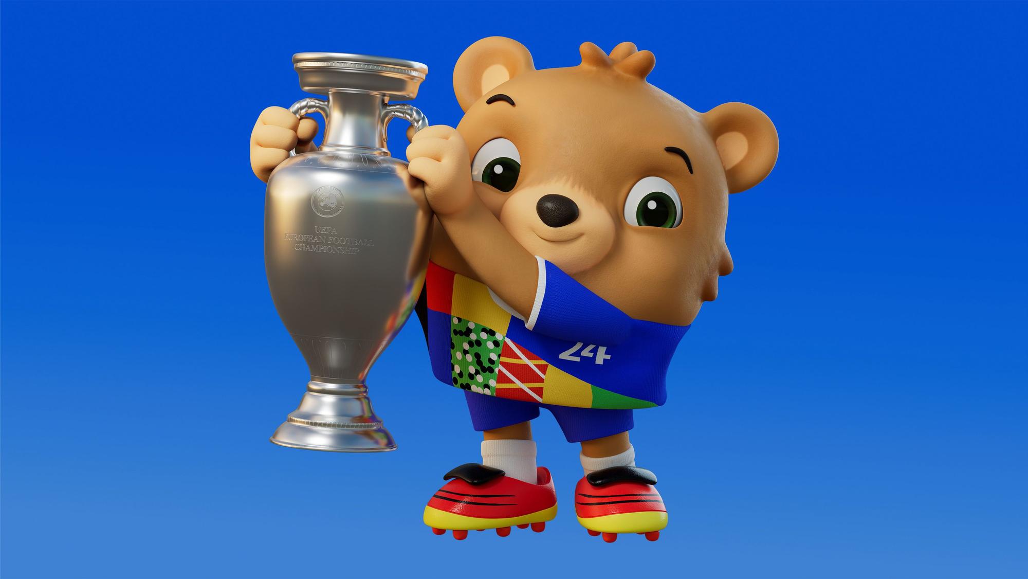 Das Maskottchen der EM 2024, ein noch namenloser Teddybär, mit dem EM-Pokal.