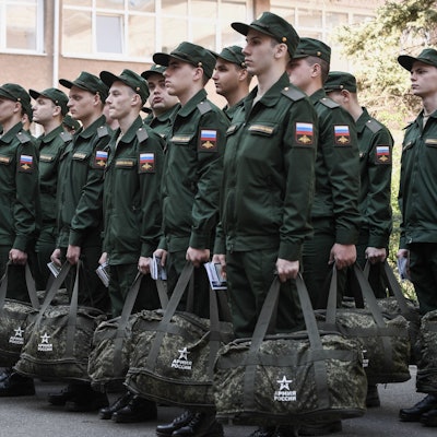 Wehrpflichtige stehen in Formation, bevor sie die Stadt verlassen, um in der russischen Armee zu dienen. Sie tragen grüne Uniform und haben eine Tasche in der Hand.