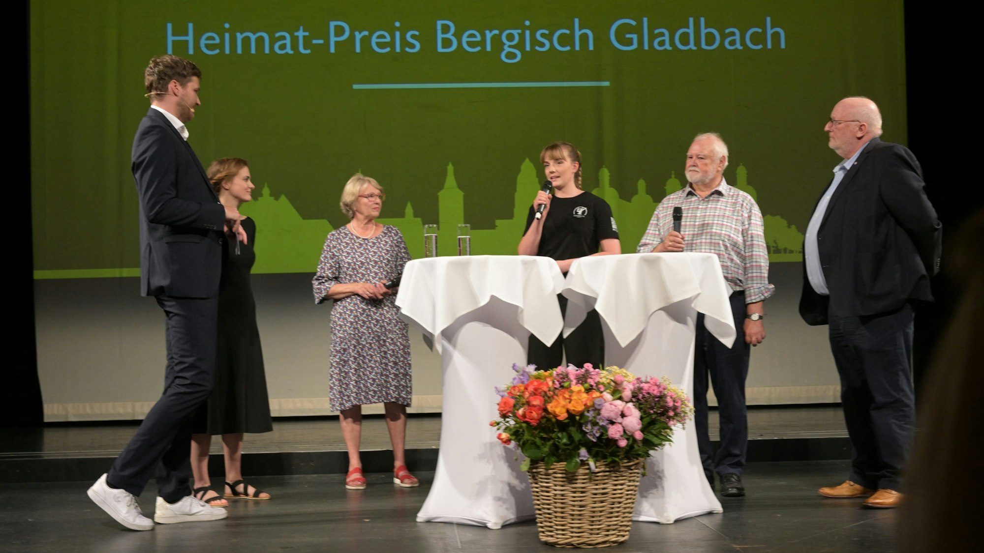 Menschen stehen auf der Bühne des Bergischen Löwen vor einer Wand mit der Aufschrift Heimat-Preis Bergisch Gladbach.