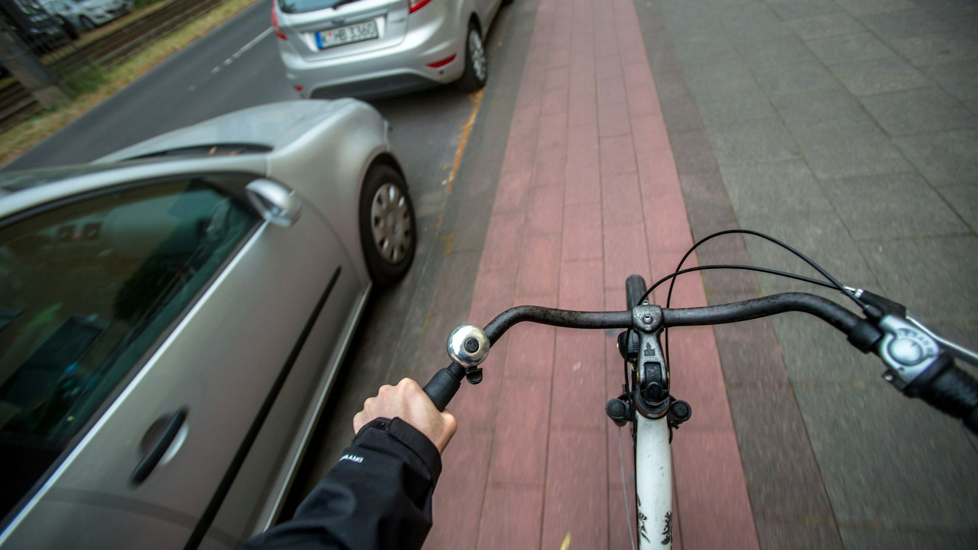 Aus der Perspektive eines Fahrradfahrers ist ein Radweg neben parkenden Autos in Köln zu sehen.