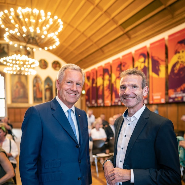 Christian Wulff trägt einen blauen Anzug mit Krawatte, Joachim Frank trägt einen schwarzen Anzug. Beide lachen in die Kamera.