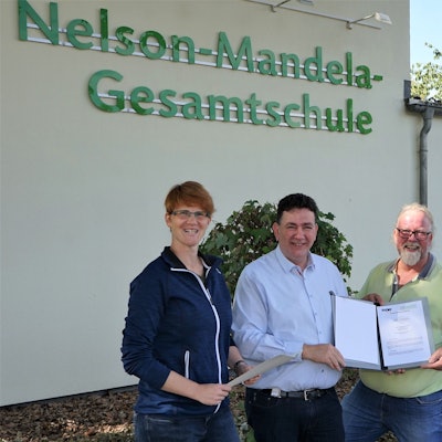 Vier Personen halten einen Vertrag vor dem Gebäude der Nelson-Mandela-Gesamtschule in die Kamera.