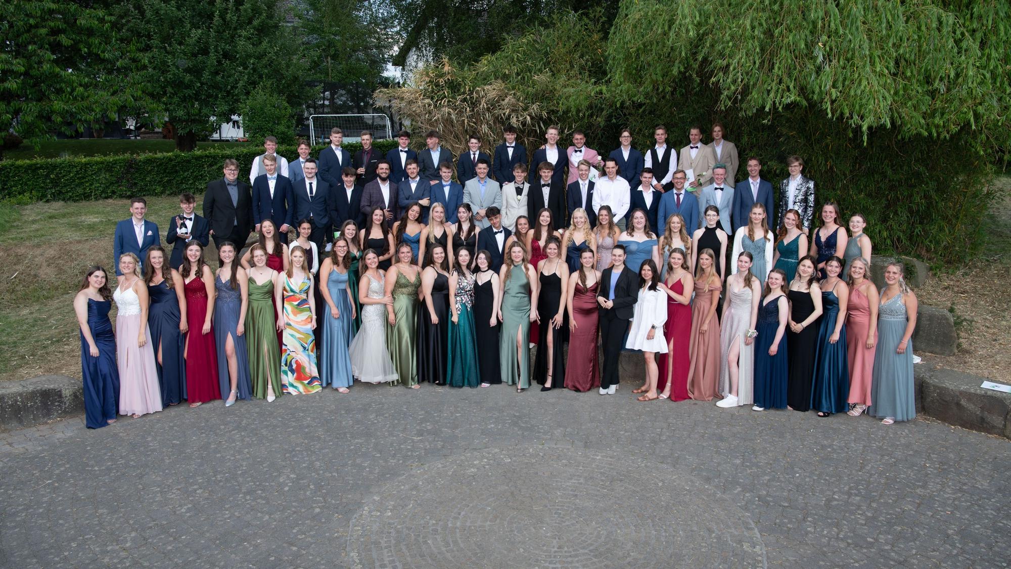 Die Abiturientinnen und Abiturienten posieren in Kleidern und Anzügen für das Foto.