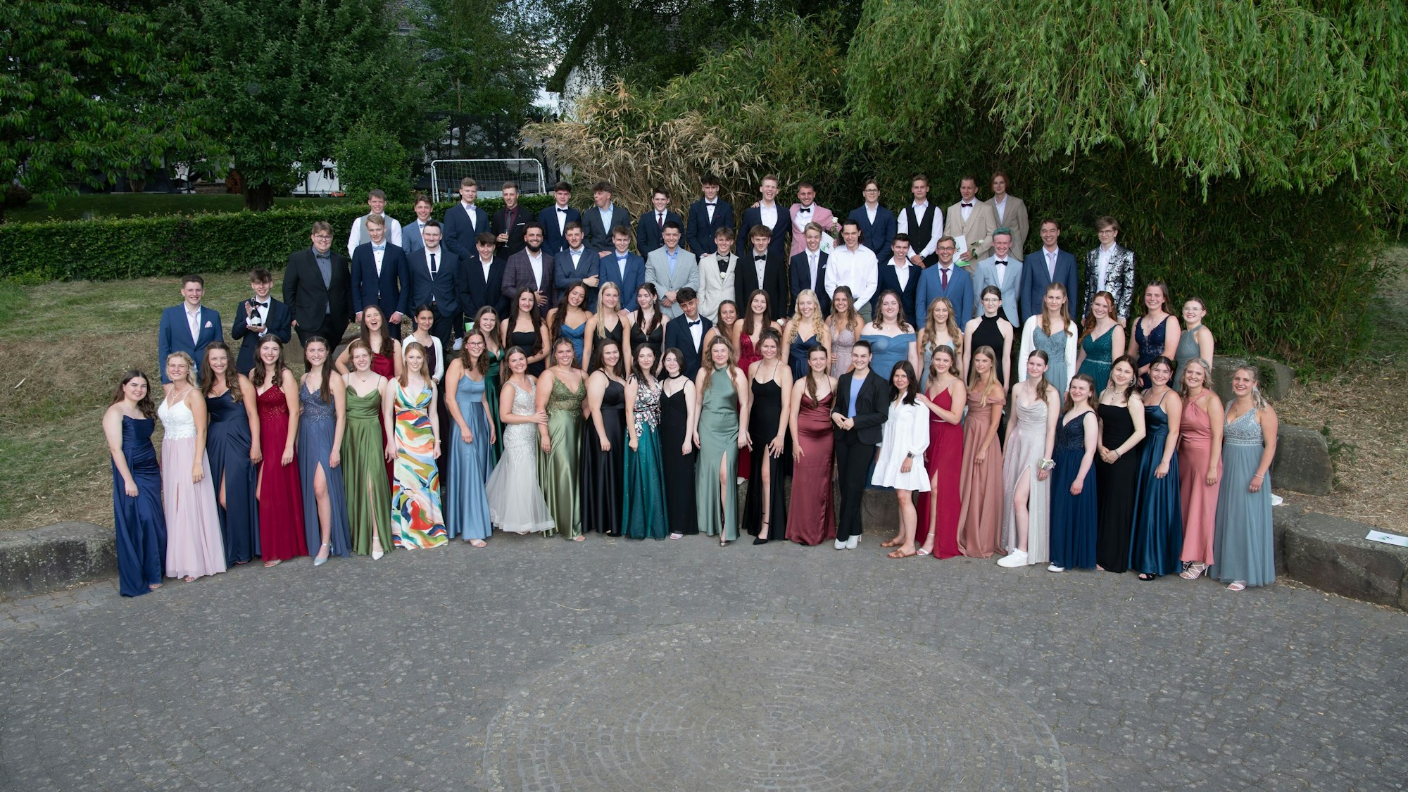 Die Abiturientinnen und Abiturienten posieren in Kleidern und Anzügen für das Foto.