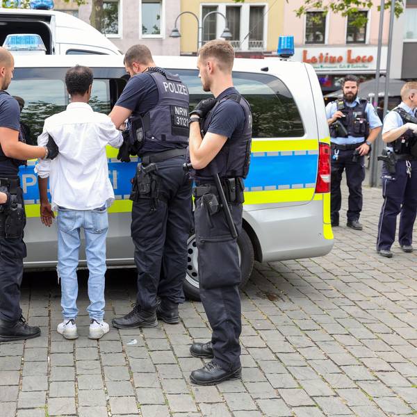 Polizisten bringen einen gefesselten, mutmaßlichen Taschendieb zu einem Streifenwagen.