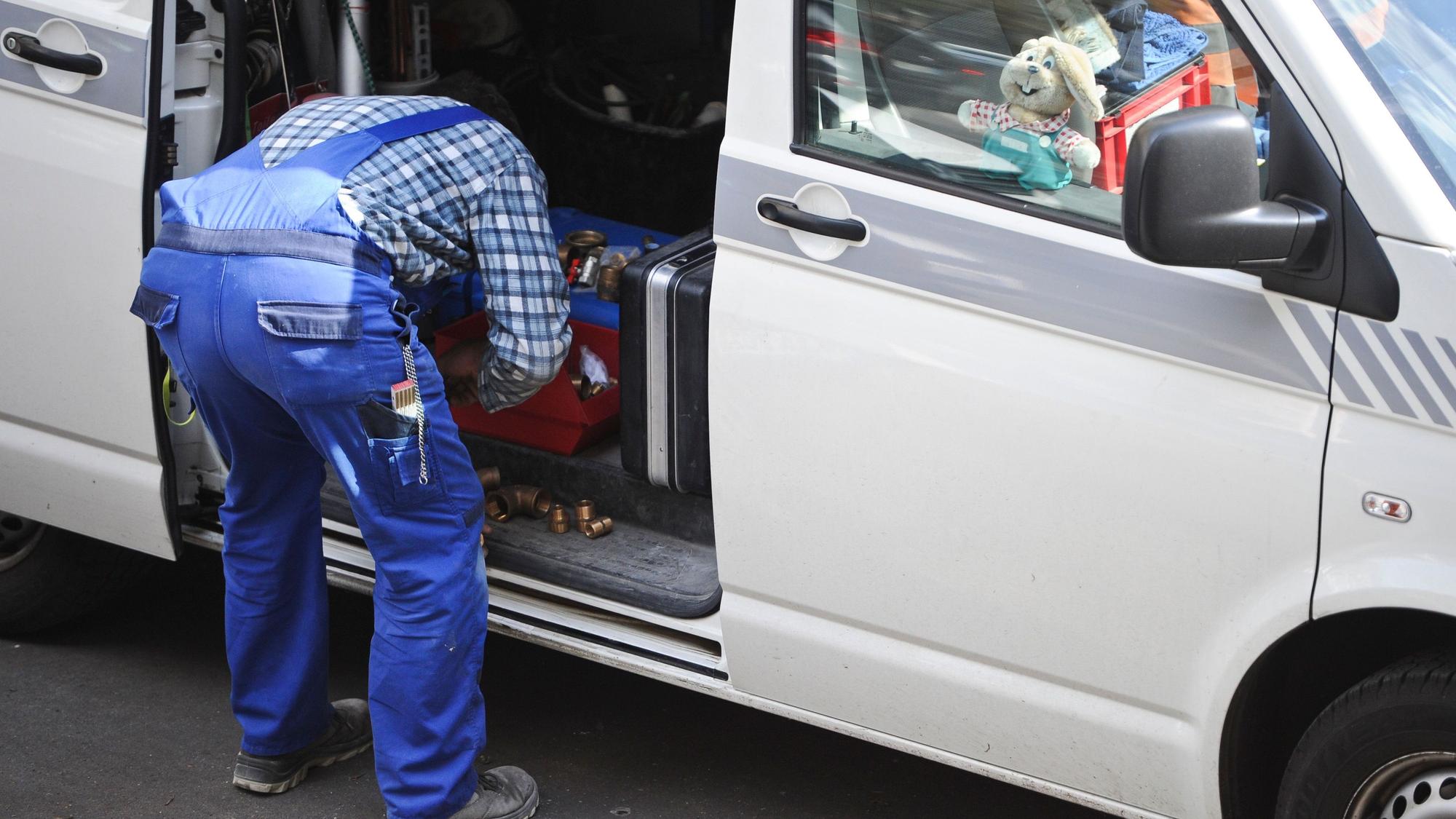 Ein Handwerker steht gebückt an seinem Auto.